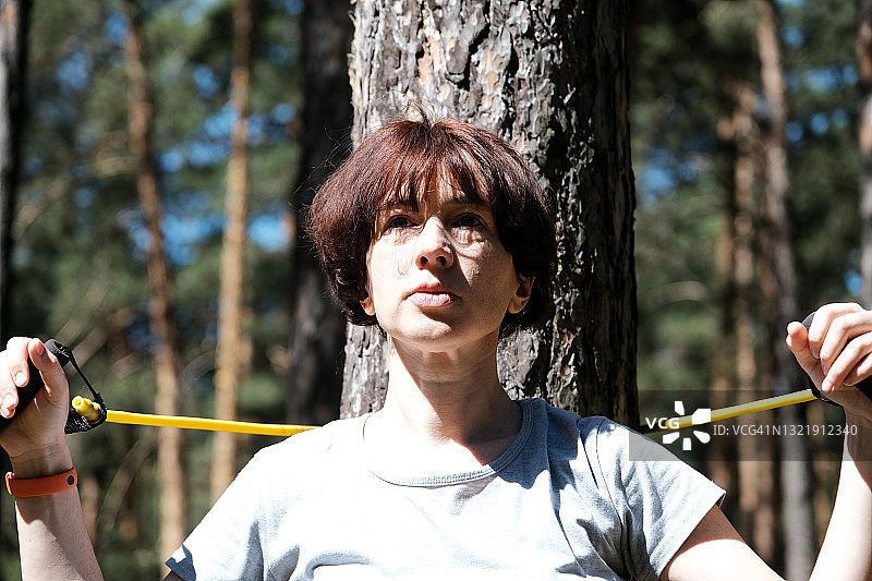 成熟的女人在松林里与阻力带一起锻炼图片素材