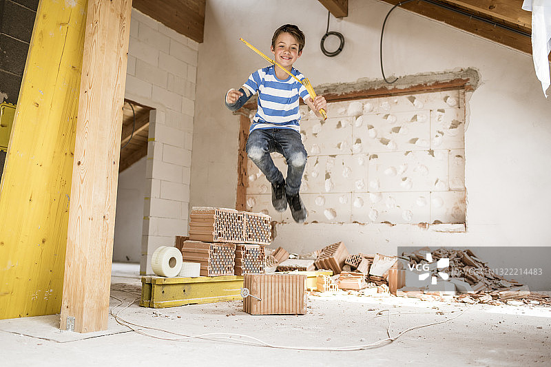 在翻修过程中，一个男孩拿着卷尺在阁楼公寓里跳来跳去图片素材