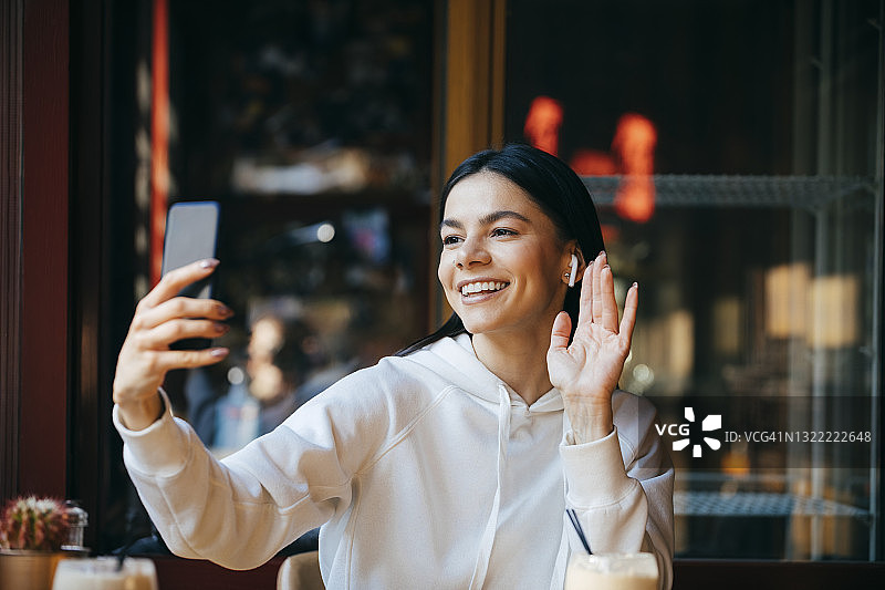 坐在咖啡馆里的快乐女人在视频通话中挥手图片素材