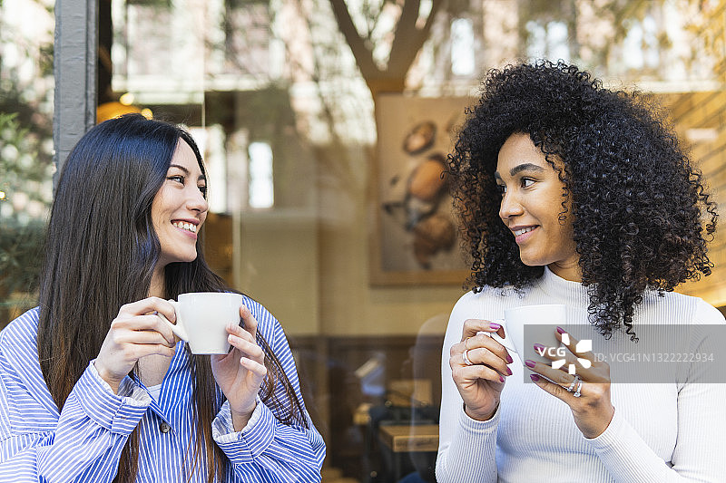 微笑的年轻女子看着女性朋友，而有咖啡在外面的酒吧图片素材