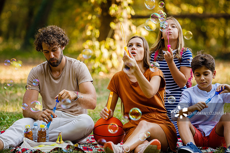 一个快乐的家庭正在享受户外野餐和吹气球。图片素材