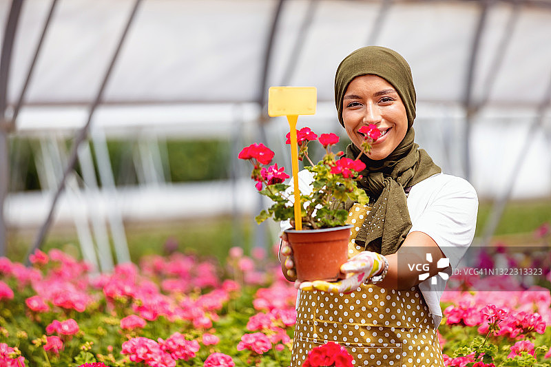 快乐的穆斯林妇女站在温室的花盆图片素材