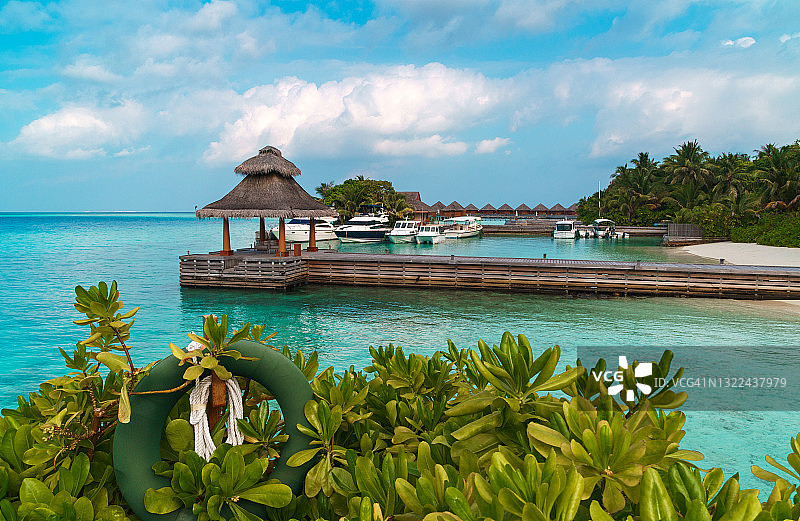 热带马尔代夫岛背景。有游艇的码头，碧绿的泻湖水域和晴朗夏日的蓝天。图片素材