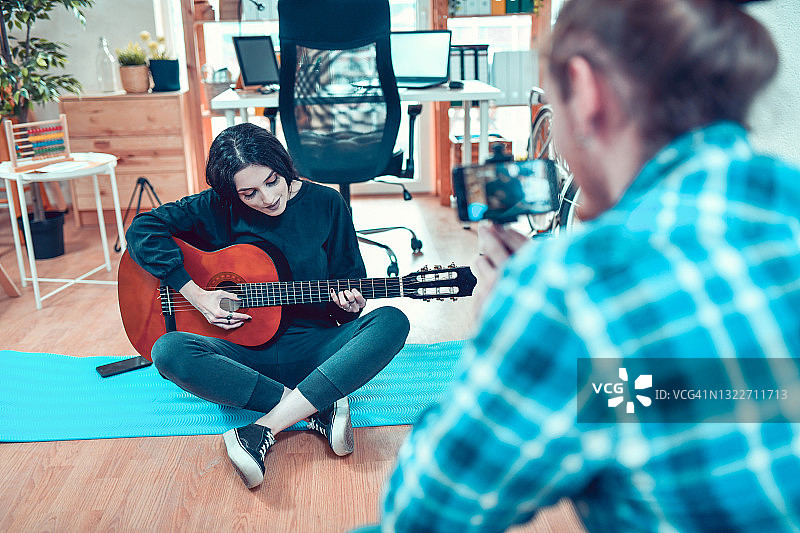 微笑的女性一边学习弹吉他，一边给男友录音图片素材