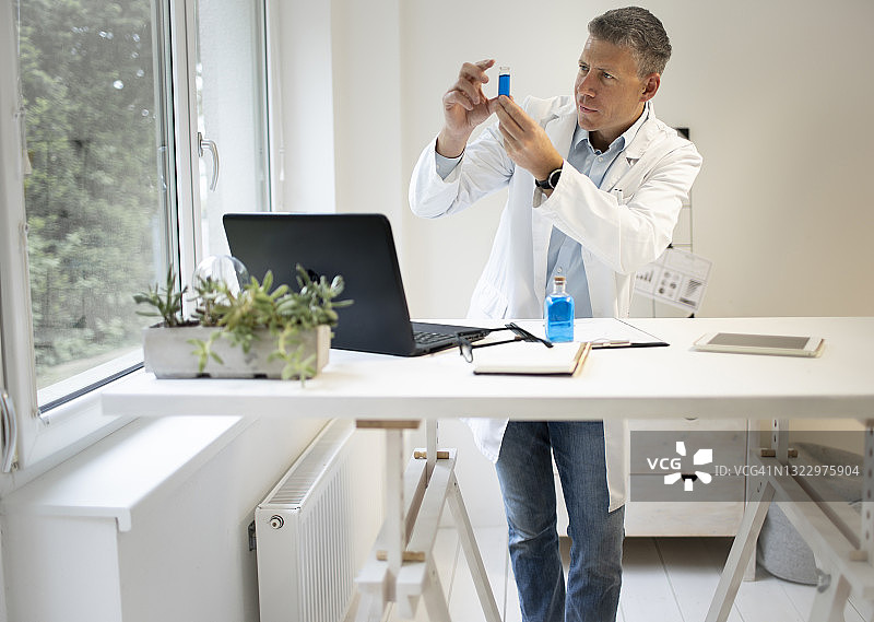 男性化学家、科学家在高台上工作，检查小瓶子里的蓝色液体图片素材