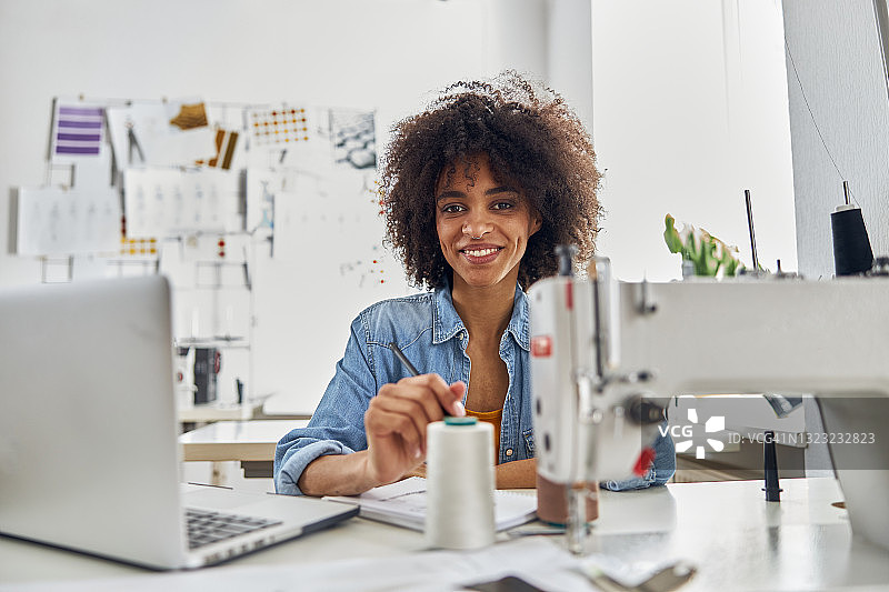 一位带着笔记本电脑微笑的非裔美国女士坐在工作室的工作场所图片素材