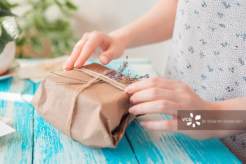 一位妇女用牛皮纸和干花包着一个包裹。手的特写镜头。接收和包装包裹的概念图片素材