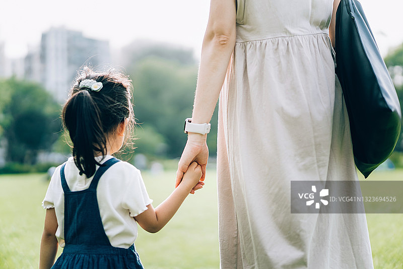 后视图，一个年轻的亚洲母亲手牵着手和她的小女儿在草坪上散步，享受家庭团聚的时间在公园。家人的爱和关心。与自然的联系概念图片素材
