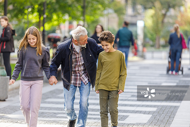 一位老人和他的孙子孙女走在城市的街道上。图片素材