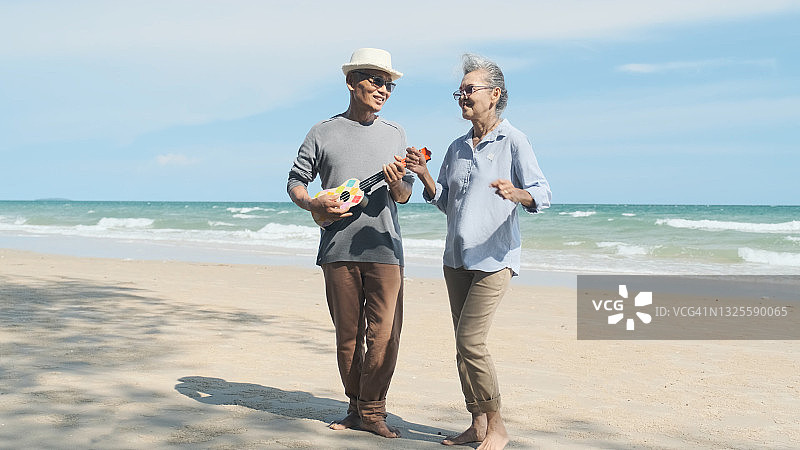 年老的亚洲夫妇弹着吉他，在海滩上愉快地跳舞图片素材