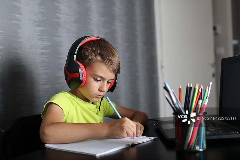 一个男孩用耳机在笔记本电脑上听课并写作图片素材