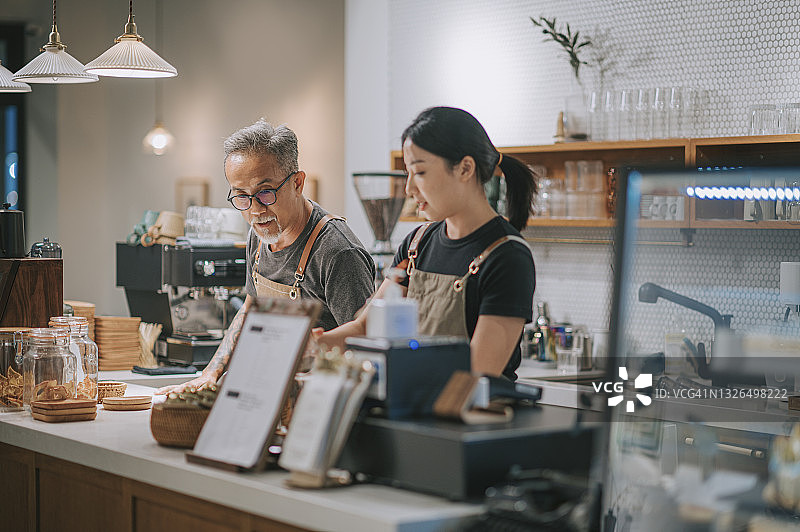 亚洲华人资深男性咖啡店老板和她的女儿清洁吧台桌子准备咖啡店开张图片素材