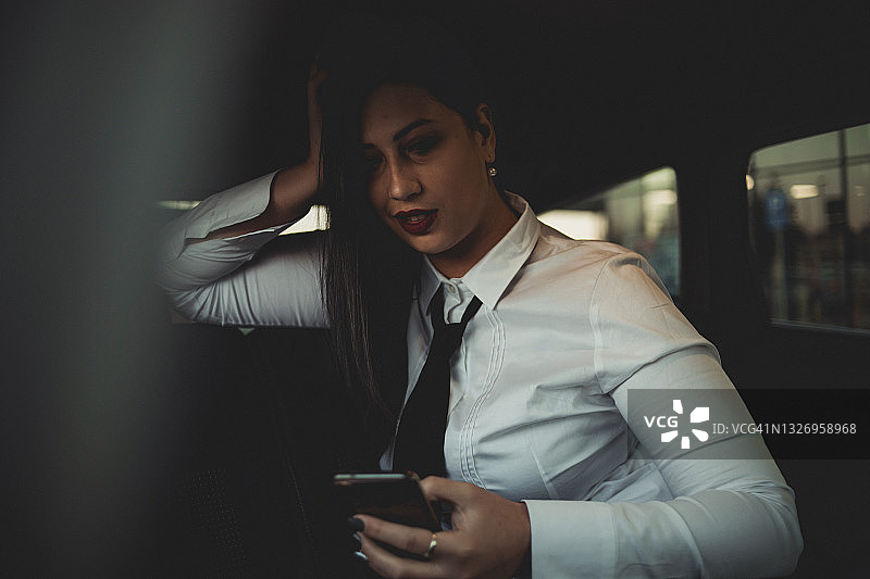 一位黑发的年轻商务妇女坐在汽车后座上，准备去参加商务会议，夕阳就在她身后。图片素材