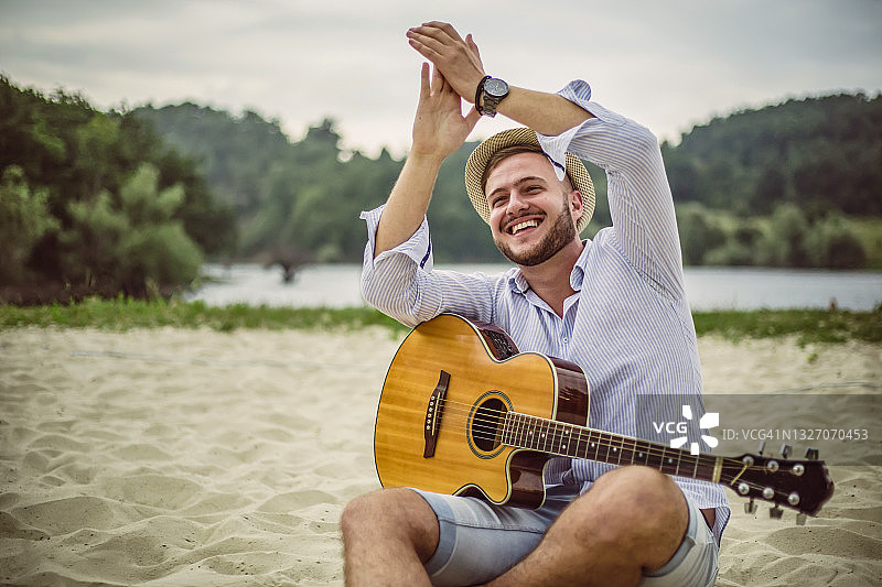 一个年轻英俊的男人在海滩上弹吉他。图片素材