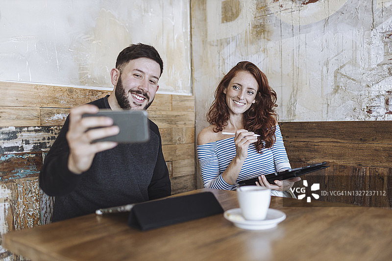 一名男子手持平板电脑与一名女同事在咖啡馆自拍图片素材
