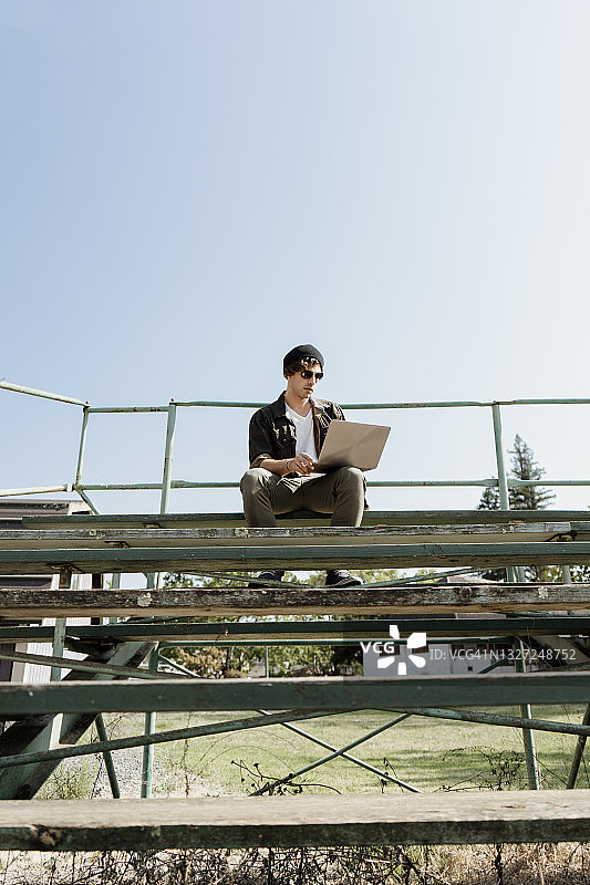 一名年轻人在阳光明媚的日子里坐在公园的台阶上使用笔记本电脑图片素材