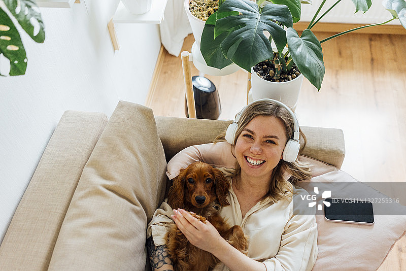 快乐的女人和可卡犬放松在客厅的沙发上图片素材