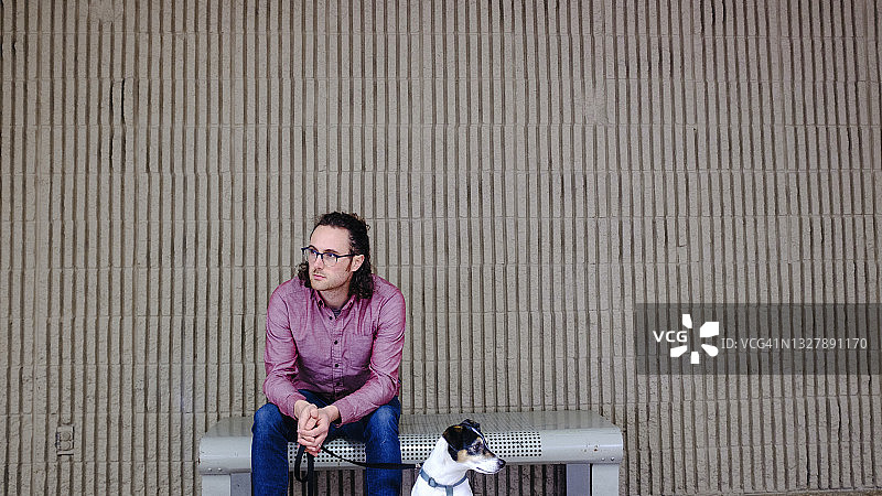 一个男人坐在长椅上，他的狗坐在他旁边。图片素材