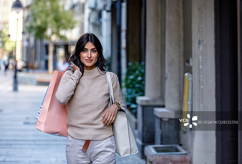 一个快乐的女人提着购物袋走在街上。图片素材