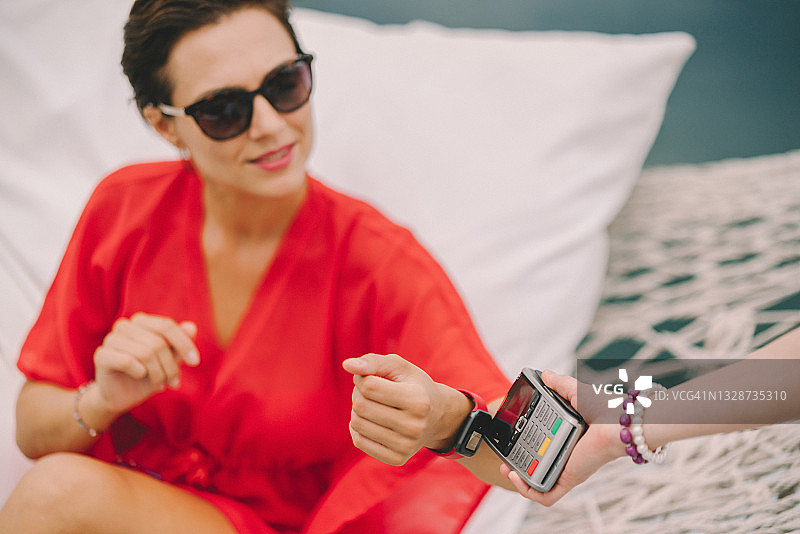 一个在海滩咖啡馆用智能手表付款的女人图片素材