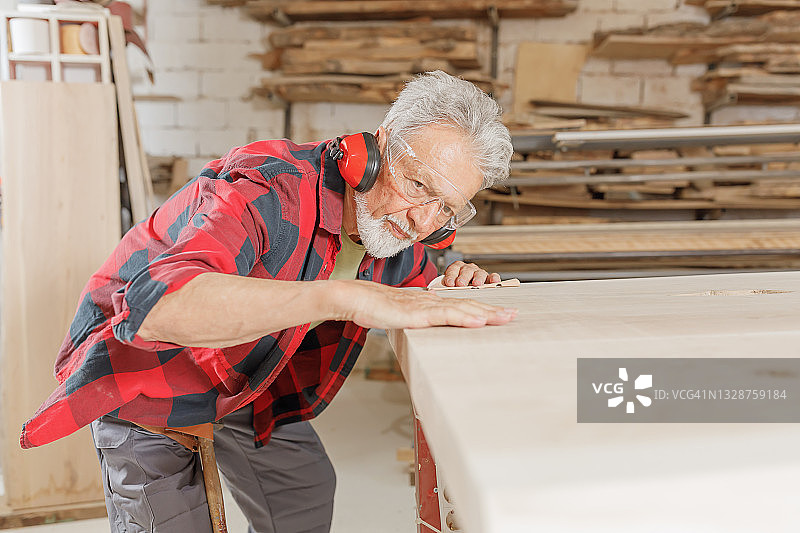 一位经验丰富的木匠正用砂纸在木工车间工作。图片素材