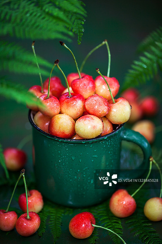 鲜湿粉红樱桃搪瓷绿色杯子，夏季概念图片素材