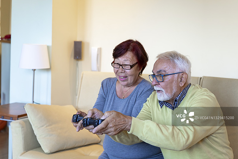 一位老年妇女和她灰白头发的丈夫在家里玩电子游戏。图片素材