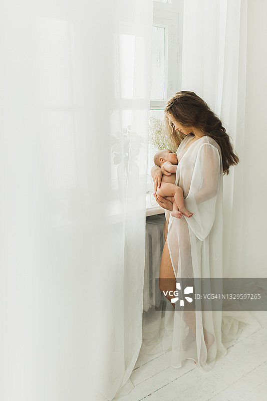美丽的年轻母亲正在给她的新生儿哺乳，抱着他的皮肤。图片素材