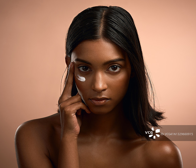 一个迷人的年轻女子的肖像应用润肤霜对一个棕色的背景图片素材
