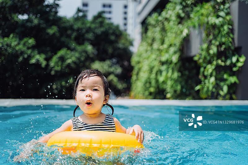 可爱的亚洲蹒跚学步的女孩在一个阳光明媚的夏天在游泳池里戏水和玩水图片素材