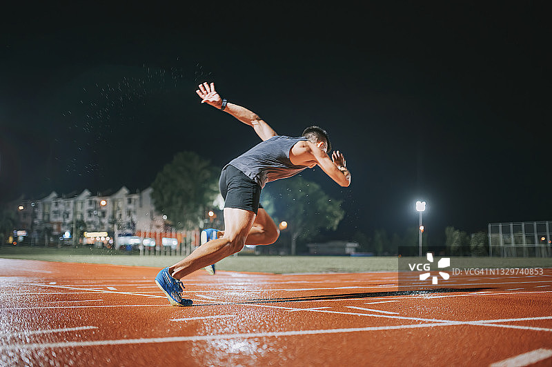 侧视图空气动力学亚洲中国男运动员在跑道上冲刺，跑向终点线在田径体育场跑道雨夜图片素材