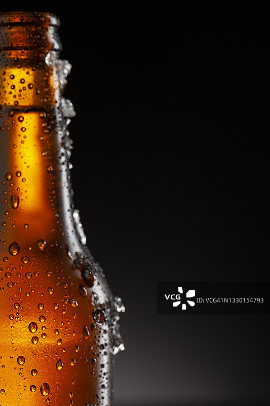 冰镇的棕色啤酒瓶覆盖着冰和水滴-凝结。用于饮料饮料产品设计模型的毛坯。站在黑色背景的黑色桌子上。图片素材