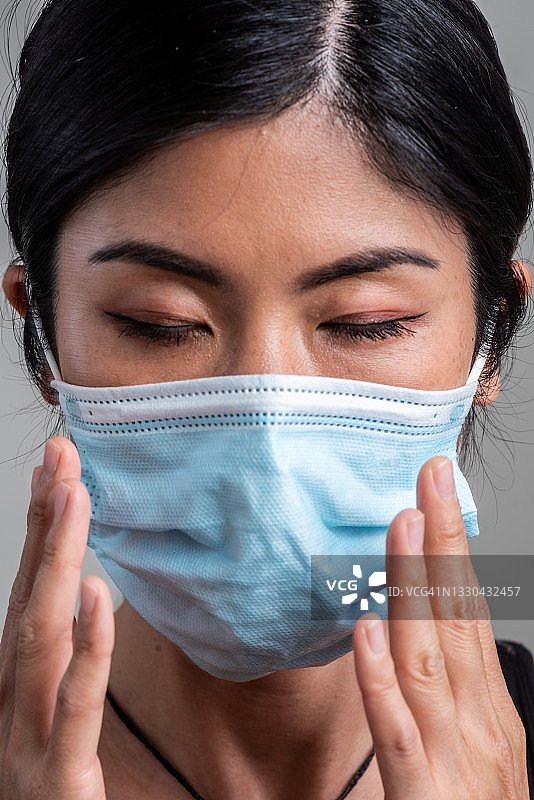 严肃的亚洲中年妇女戴着防护外科口罩俯视着灰色背景图片素材