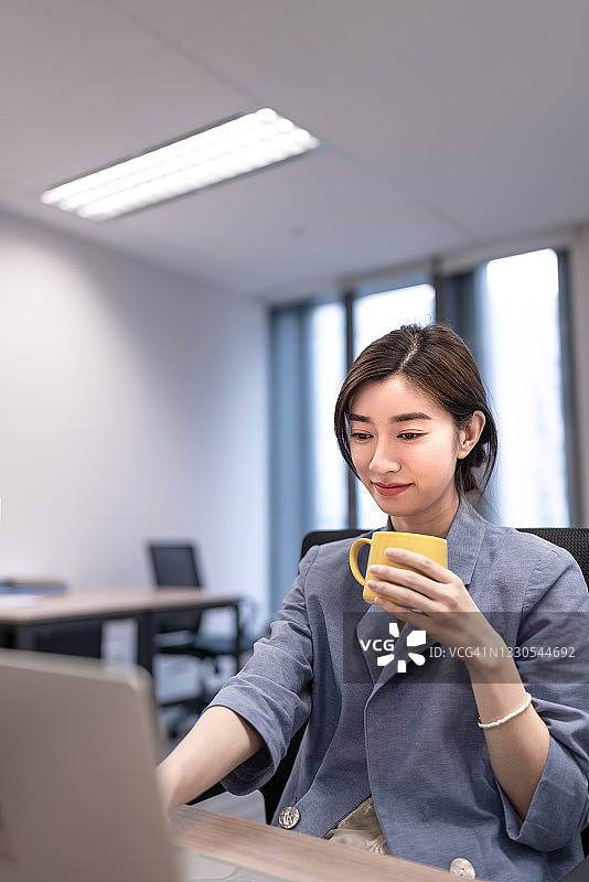 商务女性一边用笔记本电脑工作一边喝咖啡。图片素材