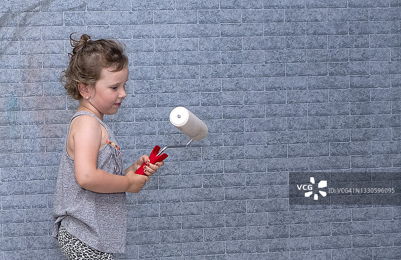 公寓装修，一个六岁的白人女孩拿着油漆滚筒。图片素材