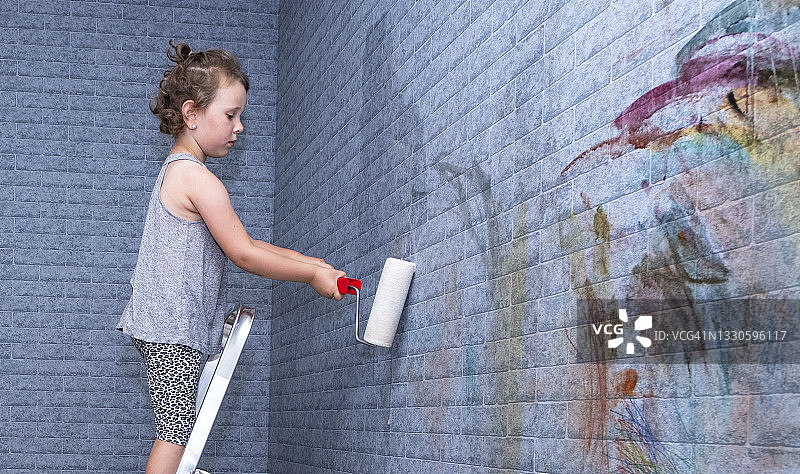 孩子，白人女孩手里拿着油漆滚筒上有个梯子。孩子正在刷墙。图片素材