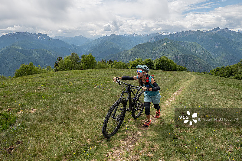 在夏天，一名女山地车手沿着小路推着自行车图片素材