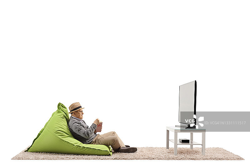 一位老人坐在豆袋椅上，一边看电视一边吃着爆米花图片素材