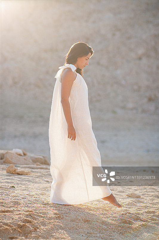 一个美丽的女人，穿着白色长裙，赤脚在细细的碎石路上行走图片素材