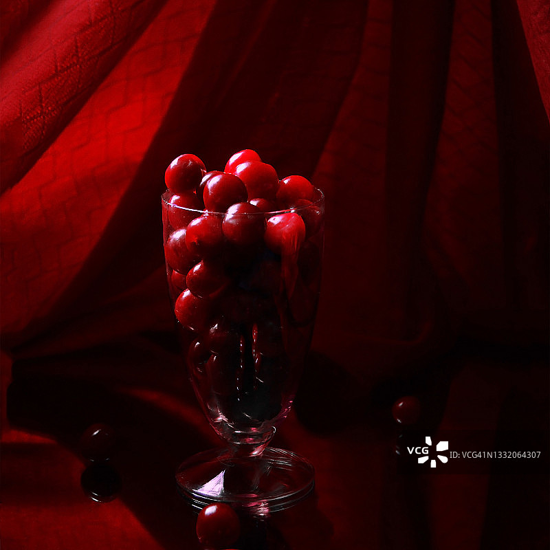 鸡尾酒杯，新鲜樱桃和它的镜像在红色背景下低调。图片素材
