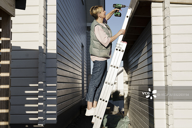 在阳光明媚的日子里，一位妇女站在梯子上修理房子图片素材