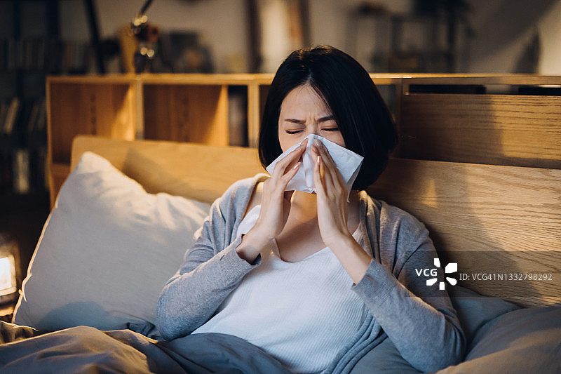 年轻的亚洲妇女患感冒和流感，躺在床上用纸巾擤鼻涕，在家休息图片素材