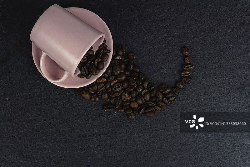 咖啡豆从粉红色的杯子溢出，在黑暗的背景下图片素材