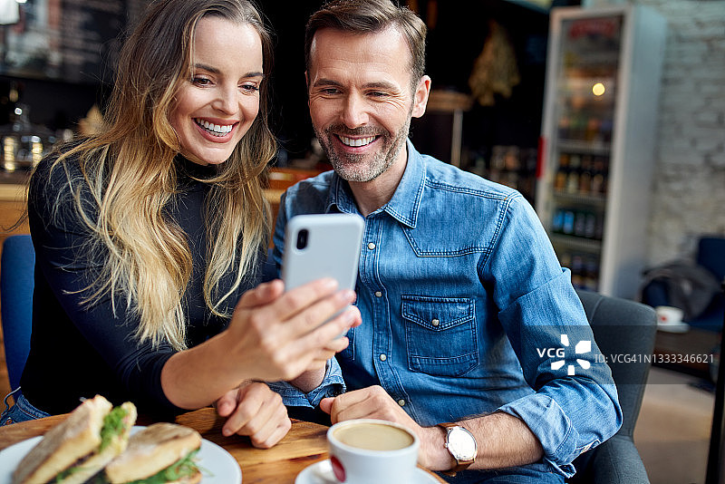 放松的情侣在咖啡馆一起浏览智能手机图片素材