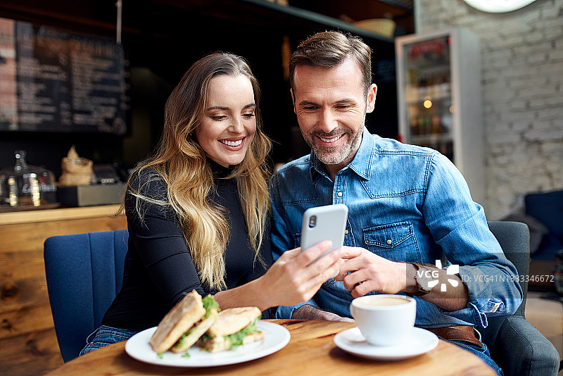 幸福的中年夫妇在咖啡馆共享电话午休图片素材