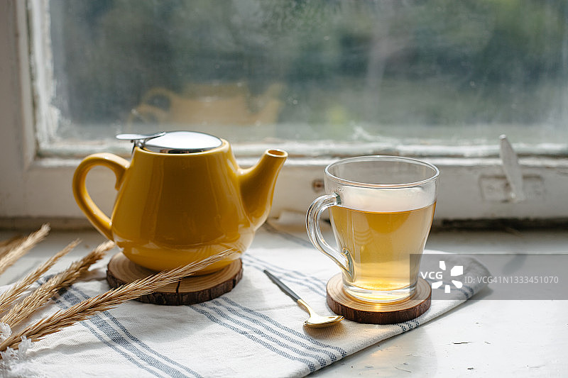 窗台上摆放着黄色的茶壶和装有花草茶的玻璃杯。图片素材