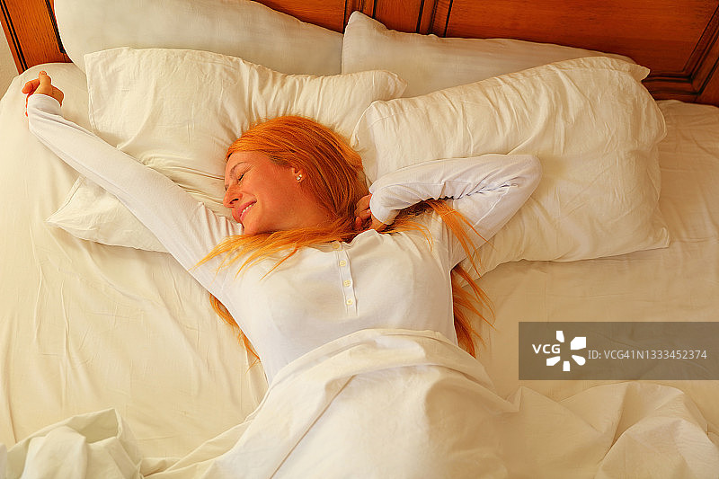 阳光明媚的早晨，一位年轻女子躺在床上伸开双臂图片素材