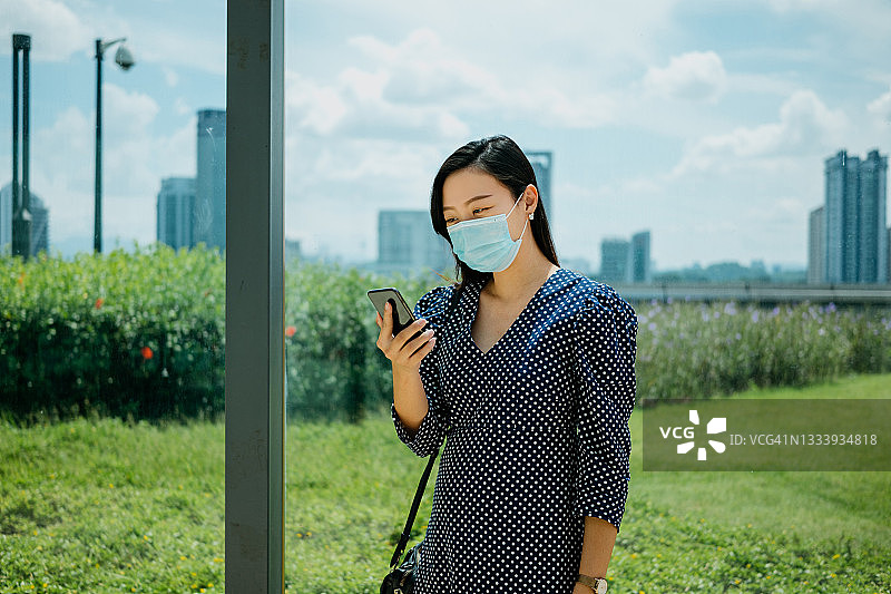 年轻的亚洲女性戴着防护口罩使用智能手机图片素材