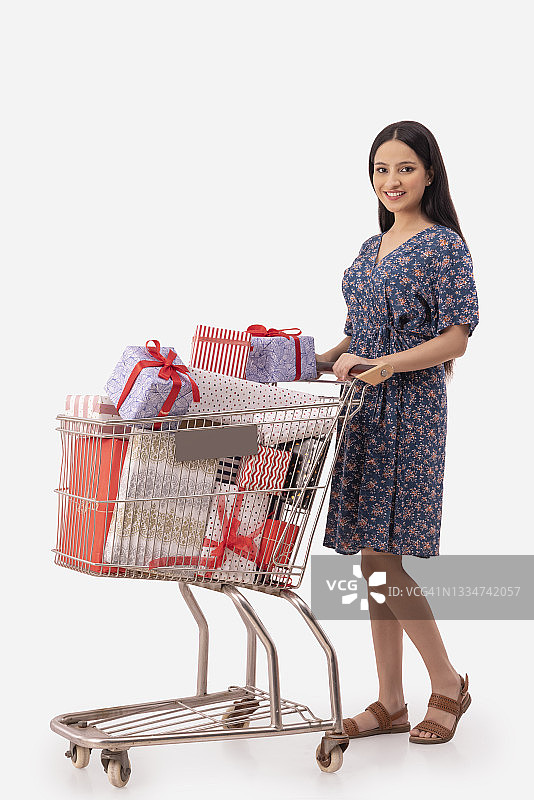 一个年轻的女人站在她装满礼物的购物车旁边。图片素材