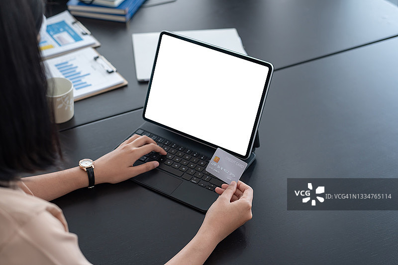 在办公室的平板电脑白屏上，一个女人手里拿着一张信用卡。模拟。图片素材
